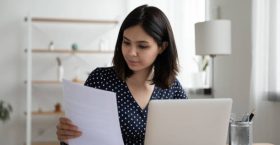 Young confident asian businesswoman work on computer at home office consider financial paperwork document. Focused Vietnamese female employee or student busy using laptop or study online.